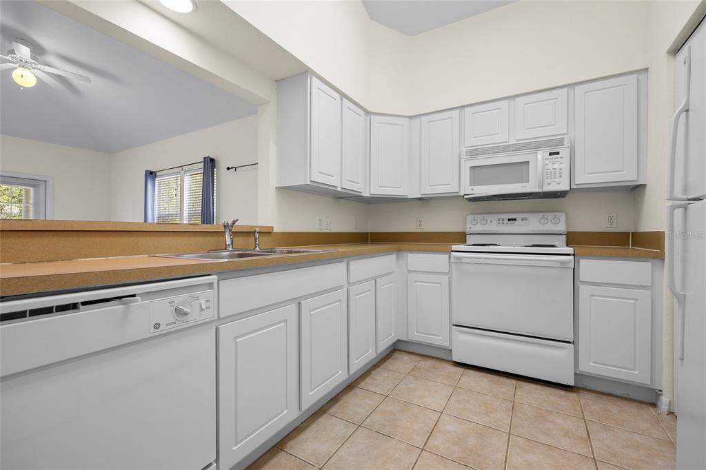 A kitchen features white cabinets, tan countertops, a white stove, and a white dishwasher — 4941 SW 91ST TERRACE UNIT N301, GAINESVILLE, FL