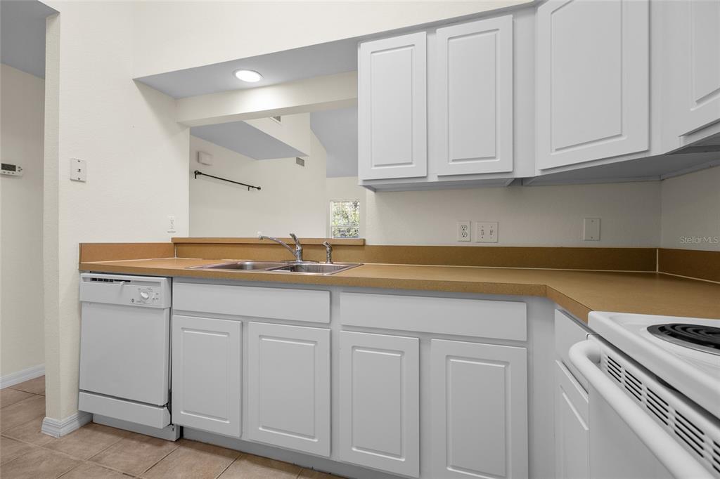 A kitchen features white cabinets, tan countertops, a double sink, and white appliances — 4941 SW 91ST TERRACE UNIT N301, GAINESVILLE, FL