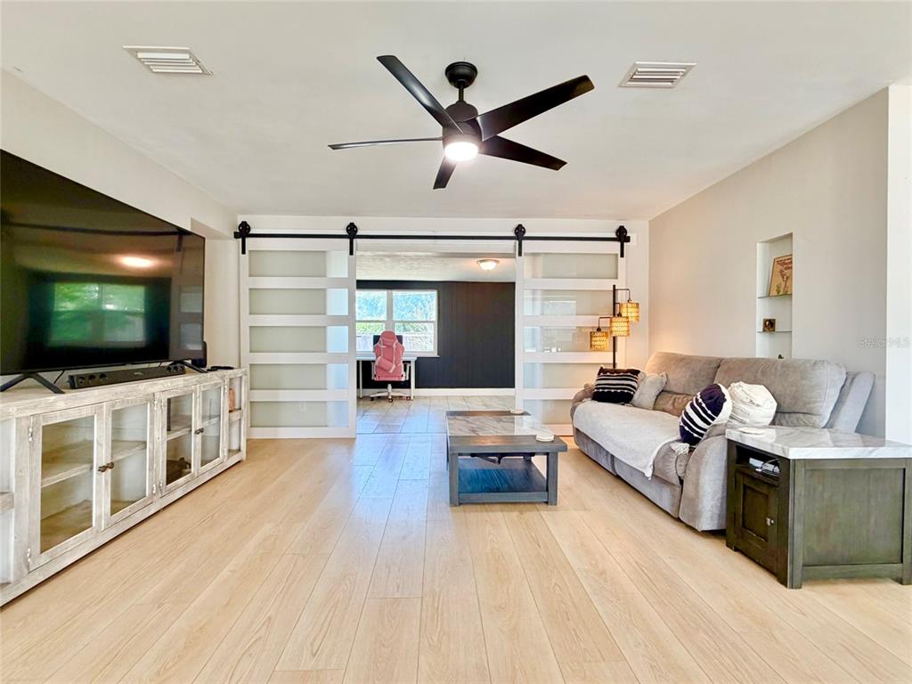 A living room features light wood flooring, a gray sofa, and sliding barn doors — 3300 58TH STREET N, ST PETERSBURG, FL