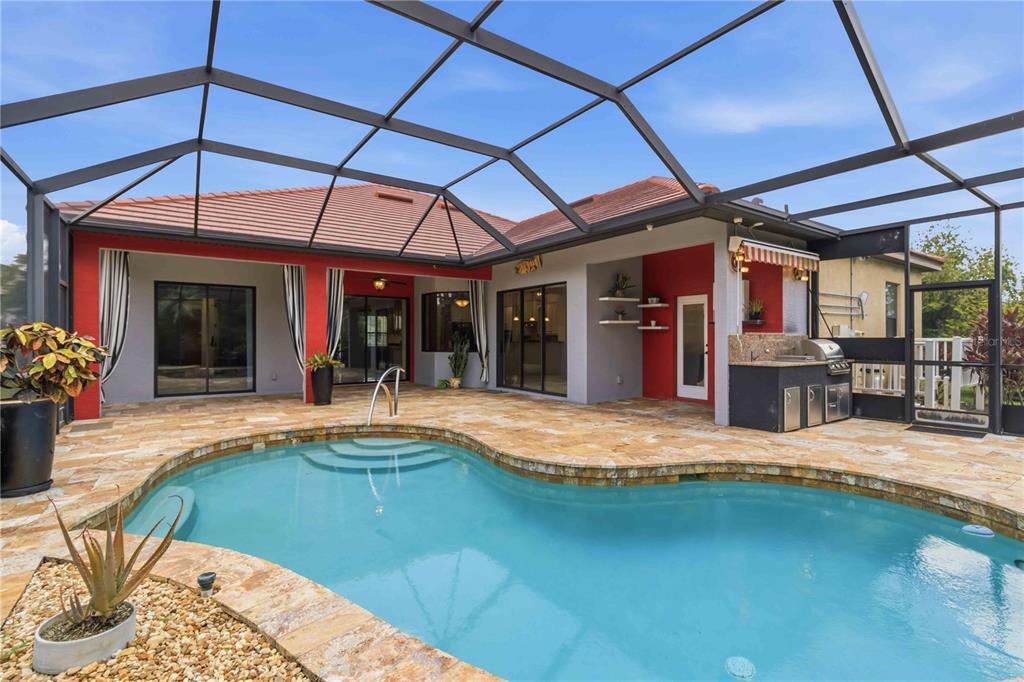 A screened-in patio features a swimming pool, stone decking, and an outdoor kitchen area — 8057 RIO BELLA PLACE, UNIVERSITY PARK, FL