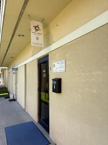 A beige exterior wall features a black door, a hanging sign, and a mailbox labeled B — PEMBROKE PINES, FL