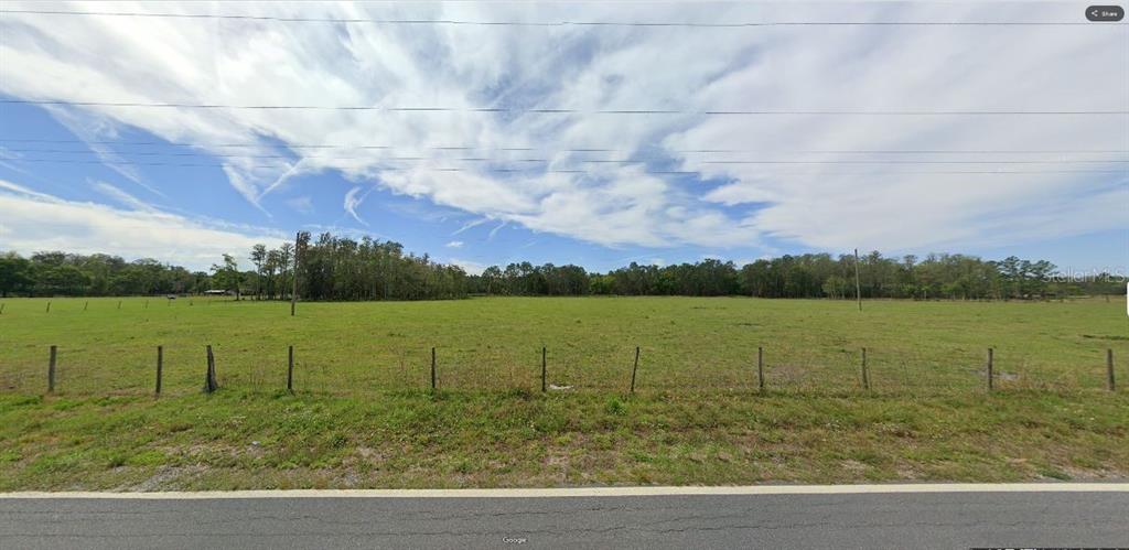 A wide, grassy, fenced-in field is bordered by a line of trees under a cloudy sky — GREEN POND RD, POLK CITY, FL