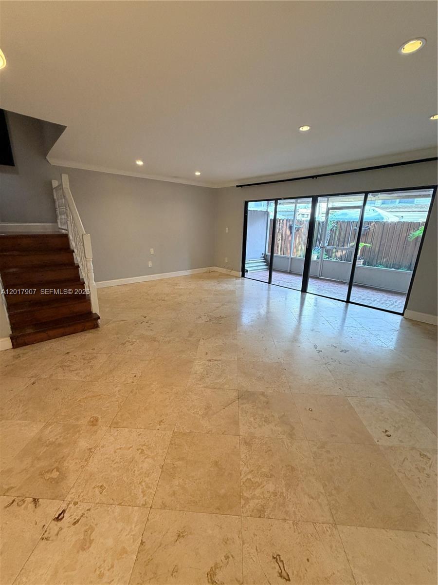 An empty living room features light-colored tile flooring, a wooden staircase, and sliding glass doors — 3300 Atlanta # 15C, Hollywood FL 33021, HOLLYWOOD, FL