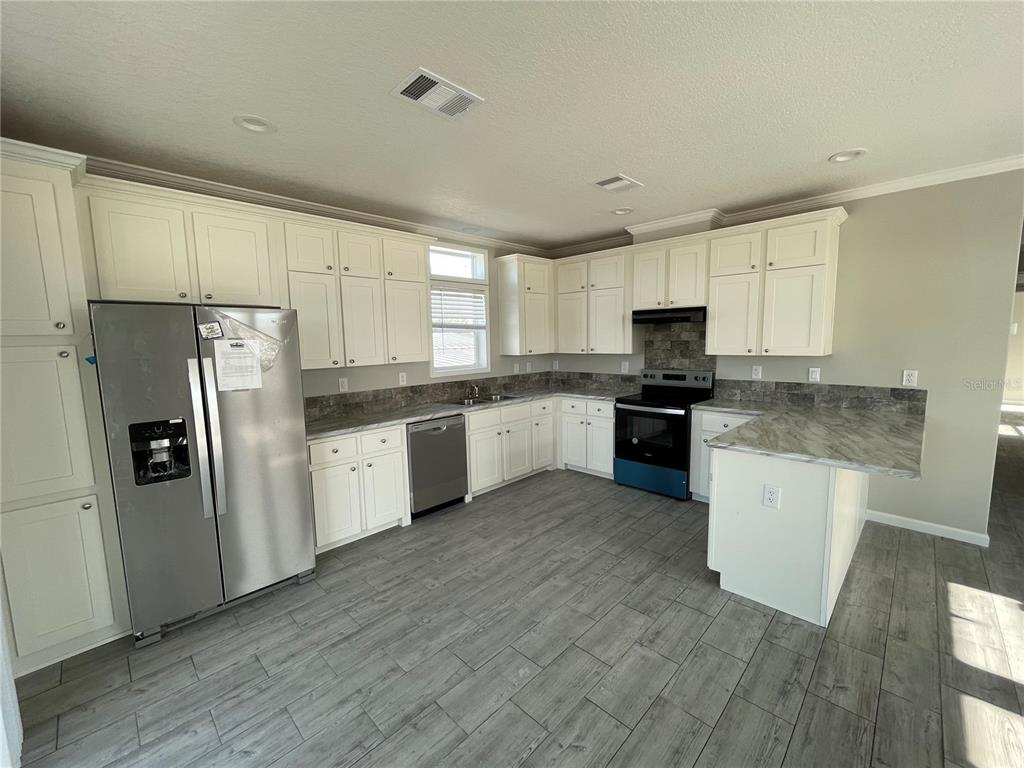 A kitchen features white cabinets, stainless steel appliances, gray countertops, and wood-look tile flooring — 715 BLACKBURN BLVD, NORTH PORT, FL
