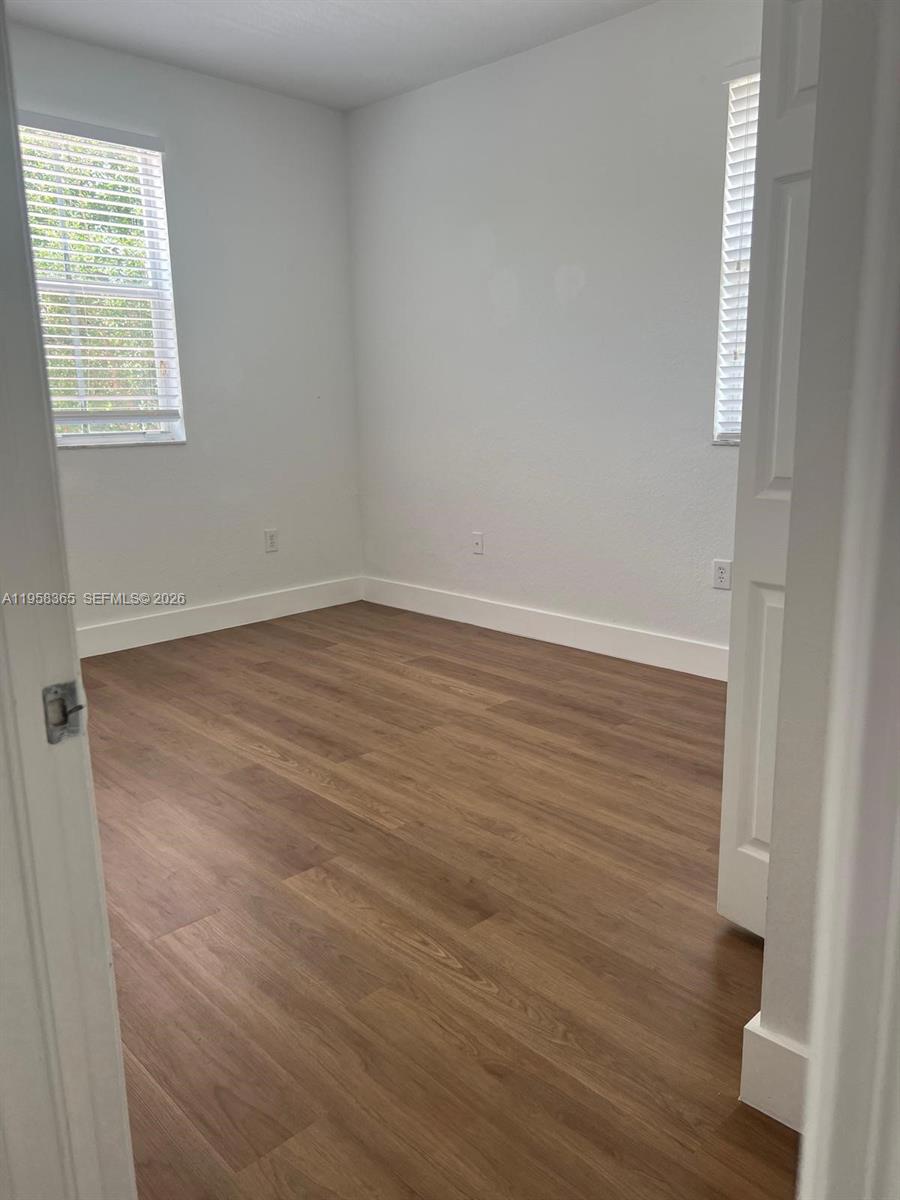 A small, empty bedroom features white walls, wood-look flooring, and two windows with blinds — 10738 NW 80th Ln, Doral FL 33178, DORAL, FL