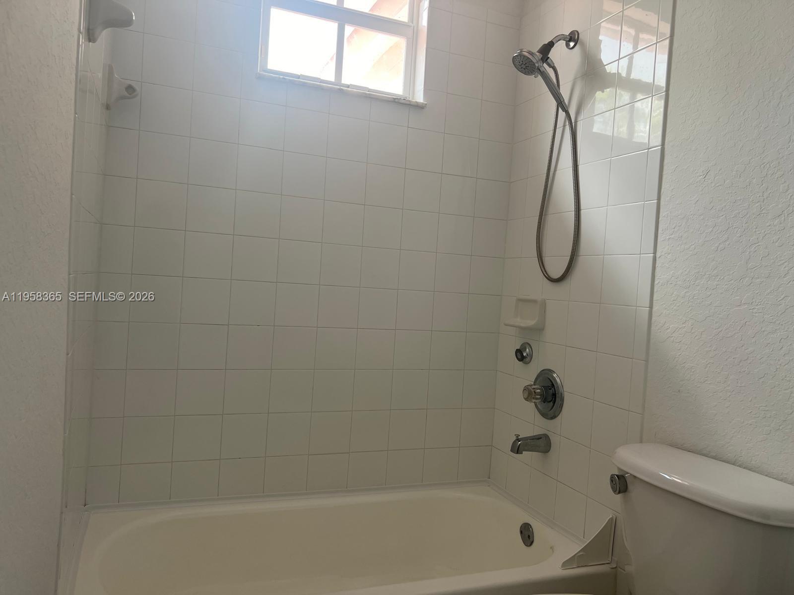 A white tiled bathtub and shower combination with a handheld showerhead and a toilet — 10738 NW 80th Ln, Doral FL 33178, DORAL, FL
