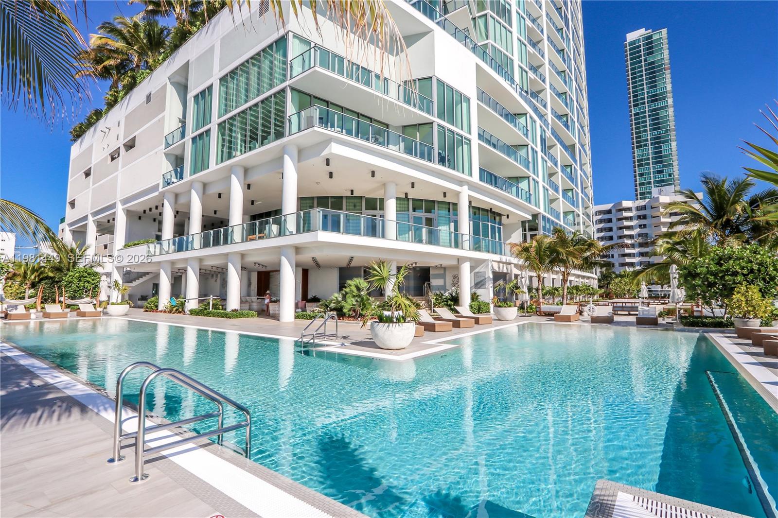 A modern high-rise building overlooks a large outdoor swimming pool with lounge chairs and palm trees — 2900 NE 7th Ave # 404, Miami FL 33137, MIAMI, FL