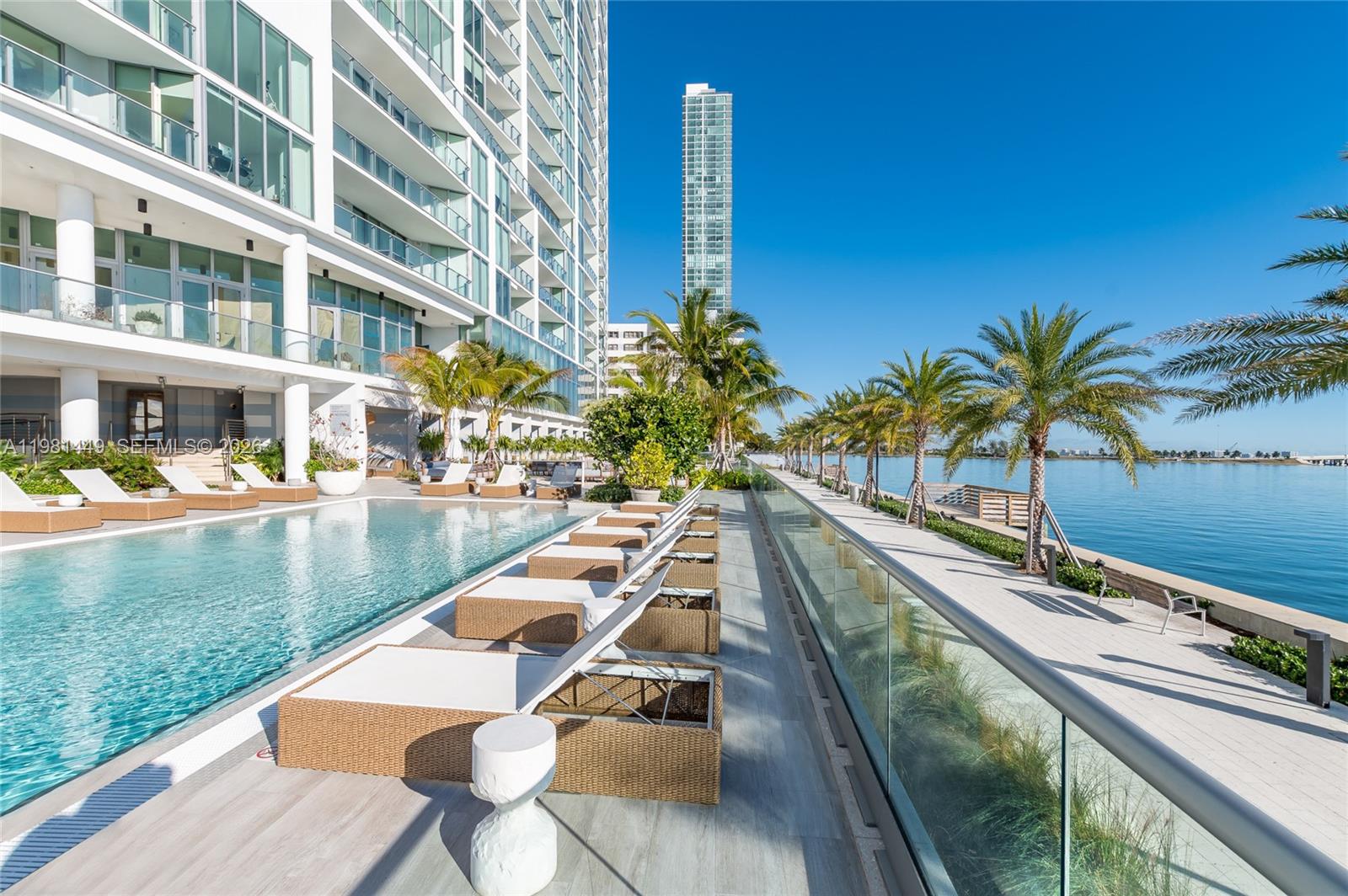A swimming pool area features lounge chairs on a deck overlooking a bay and skyscrapers — 2900 NE 7th Ave # 404, Miami FL 33137, MIAMI, FL