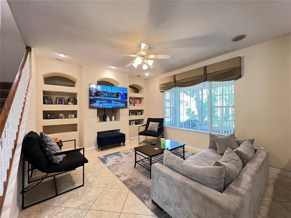 A living room features a built-in media wall, a ceiling fan, and a large window — 1607 TAIL FEATHER DRIVE, KISSIMMEE, FL