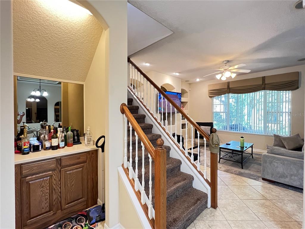 A carpeted staircase with a wooden railing sits beside a wet bar and living area — 1607 TAIL FEATHER DRIVE, KISSIMMEE, FL