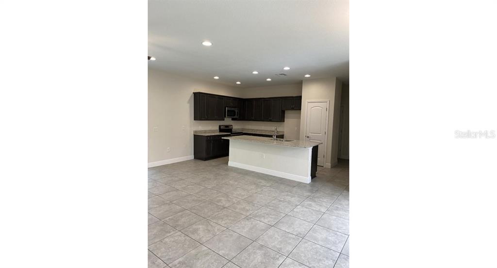 A kitchen with dark cabinets, a granite-topped island, and light-colored tile flooring — 7724 SWISS AVENUE, NORTH PORT, FL