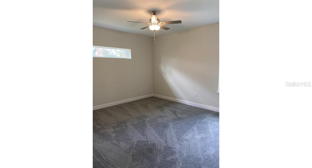A bedroom with beige walls, gray carpet, and a ceiling fan with a light fixture — 7724 SWISS AVENUE, NORTH PORT, FL