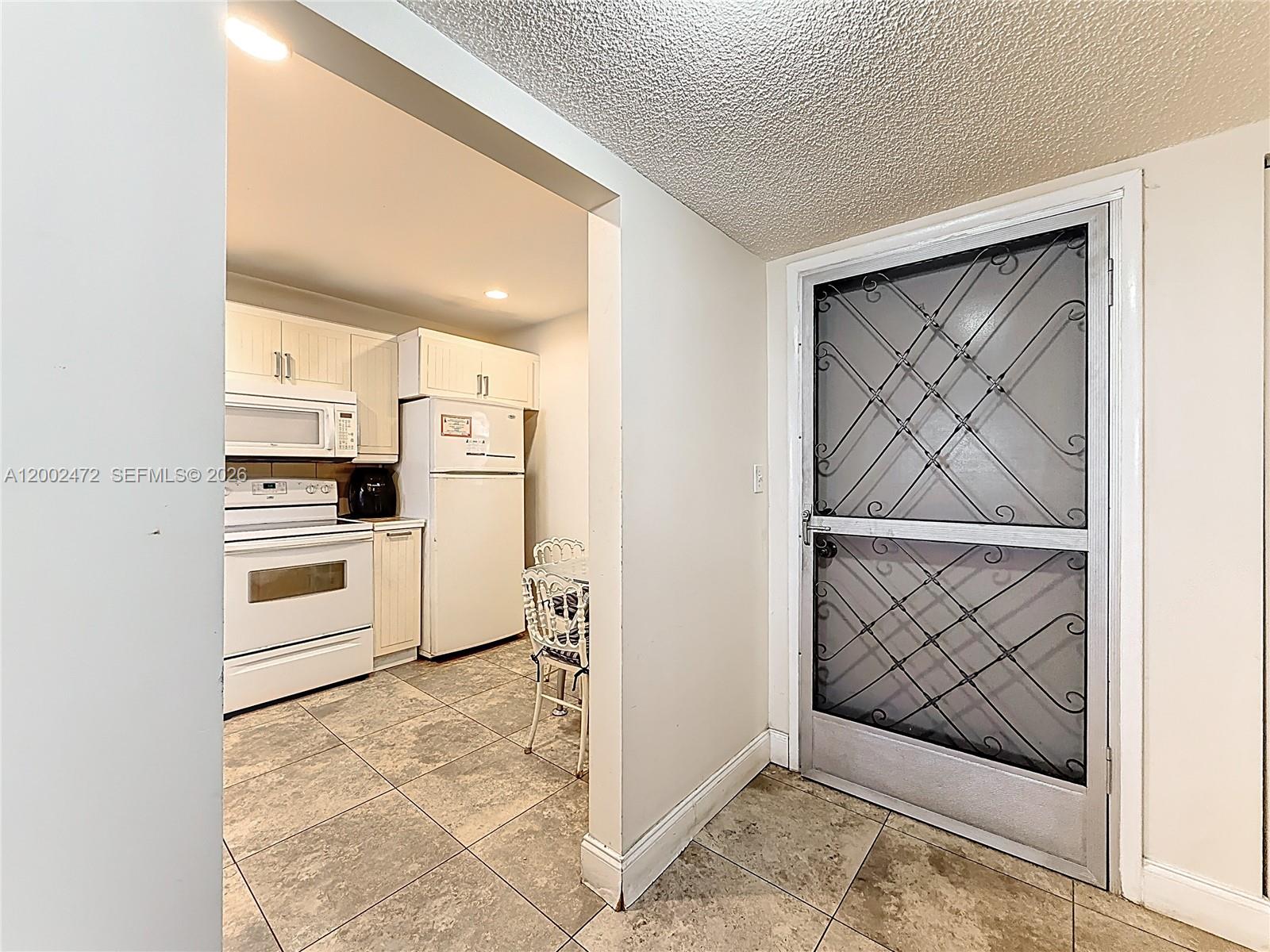 A kitchen with white appliances and cabinets is visible through an opening next to a door — 410 SE 2nd St # 115, Hallandale Beach FL 33009, HALLANDALE BEACH, FL