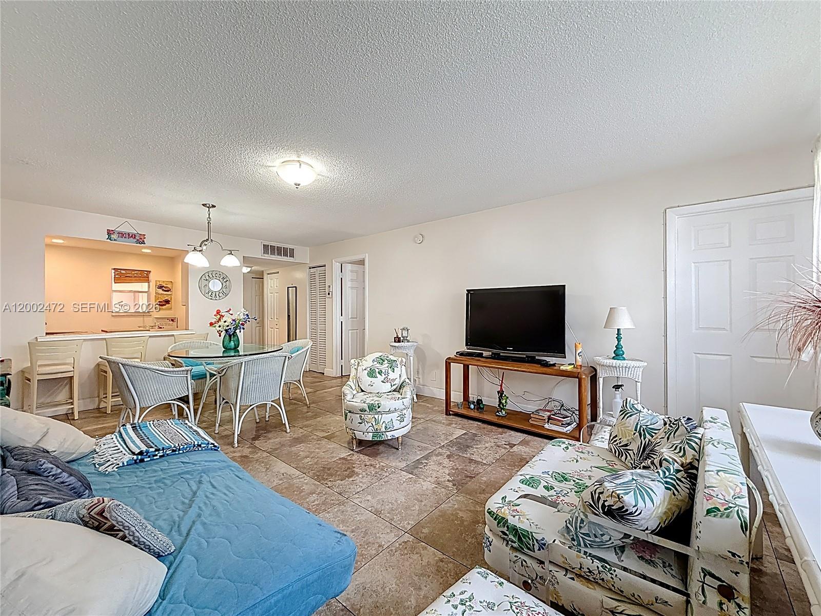 A living room features tile flooring, a television on a wooden stand, and floral furniture — 410 SE 2nd St # 115, Hallandale Beach FL 33009, HALLANDALE BEACH, FL