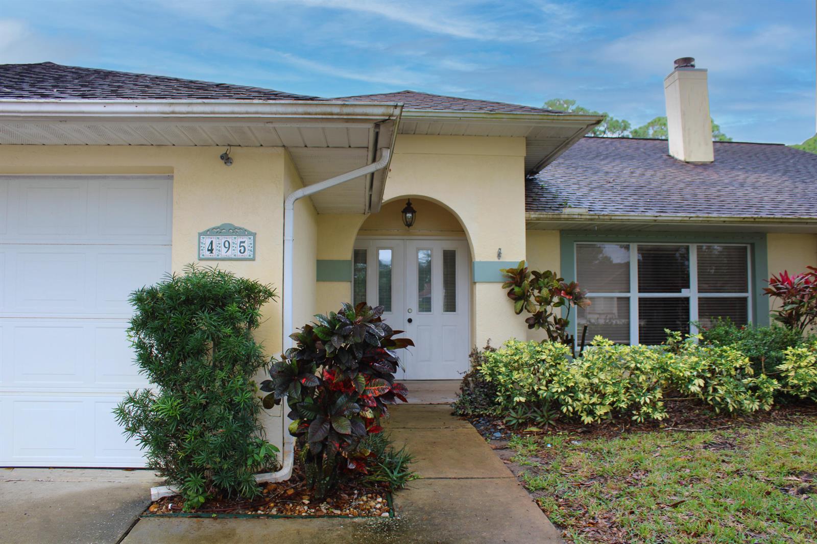 A single-story house with a white garage door, arched entryway, and landscaped front yard — 495 11th Court, Vero Beach FL 32962, VERO BEACH, FL