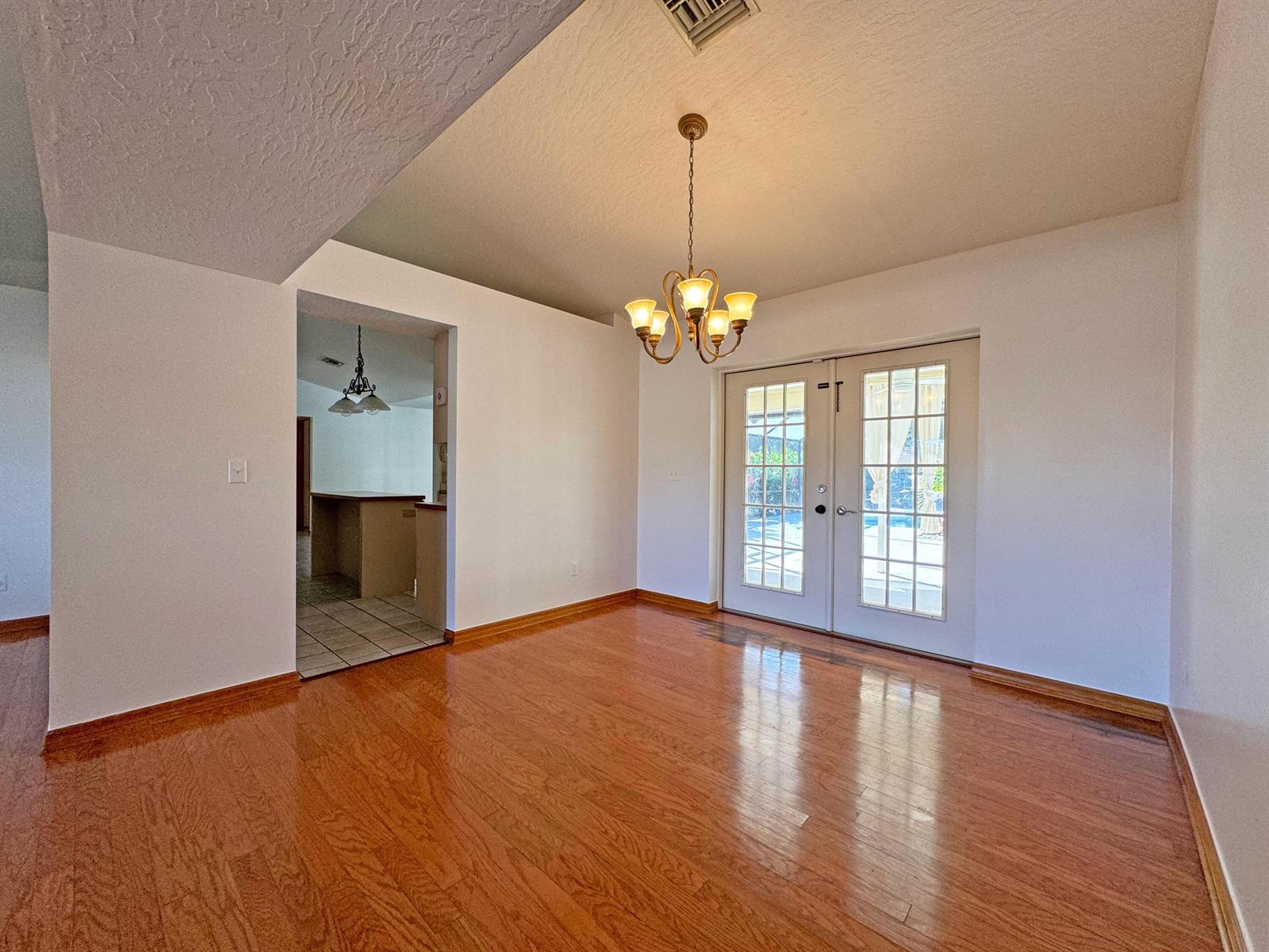 An empty dining room with hardwood floors, a chandelier, and double glass doors to a patio — 495 11th Court, Vero Beach FL 32962, VERO BEACH, FL