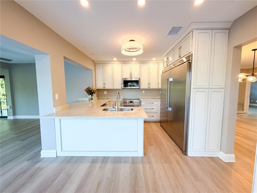 A kitchen features white cabinetry, stainless steel appliances, a peninsula, and light wood flooring — 410 SW 56TH AVENUE, PLANTATION, FL