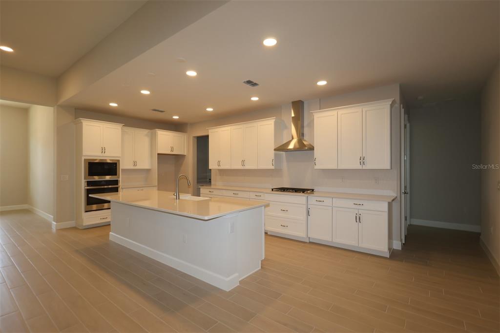 A modern kitchen features white cabinetry, a large island with a sink, and light flooring — 3270 WOLF LAKE AVENUE, APOPKA, FL