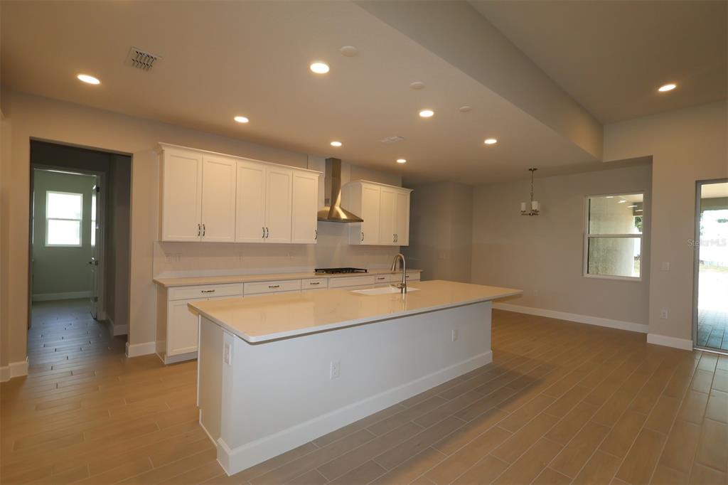 A modern kitchen features white cabinetry, a large central island, and light-colored tile flooring — 3270 WOLF LAKE AVENUE, APOPKA, FL