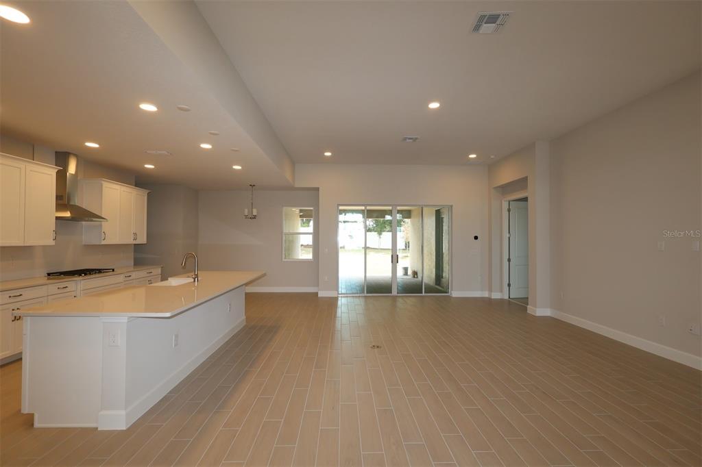 A modern open-concept kitchen and living area with light wood-look tile flooring and sliding doors — 3270 WOLF LAKE AVENUE, APOPKA, FL