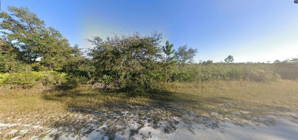 A view of a vacant, sandy lot with scattered trees and low-lying vegetation under blue skies — SARASOTA DRIVE, INDIAN LAKE ESTATES, FL