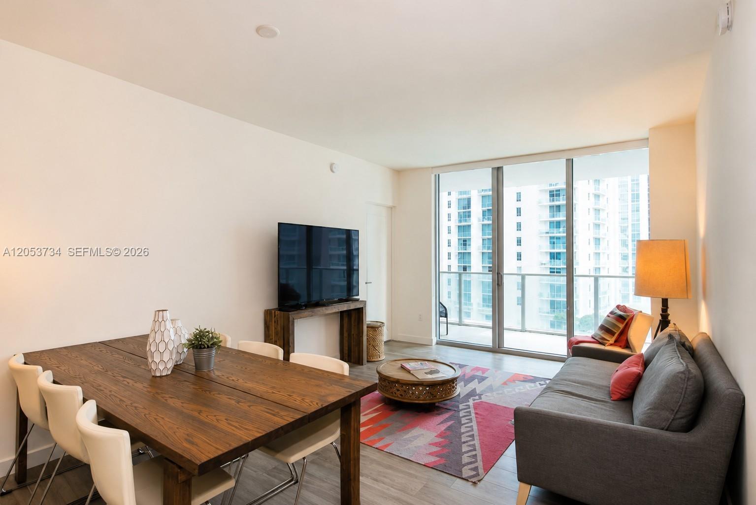 A living and dining area features a wooden table, gray sofa, and floor-to-ceiling windows — 1100 S Miami Ave # 1711, Miami FL 33130, MIAMI, FL