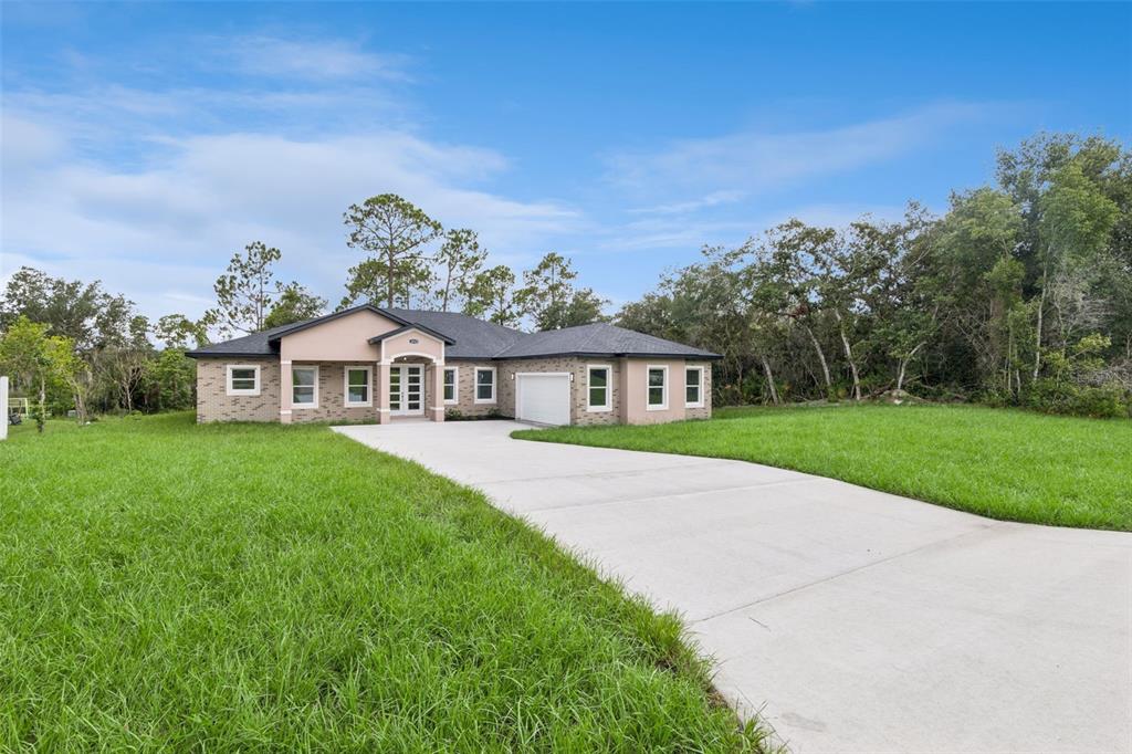 A single-story brick house with a concrete driveway and a grassy yard under a blue sky — 2043 WATERSEDGE DRIVE, DELTONA, FL