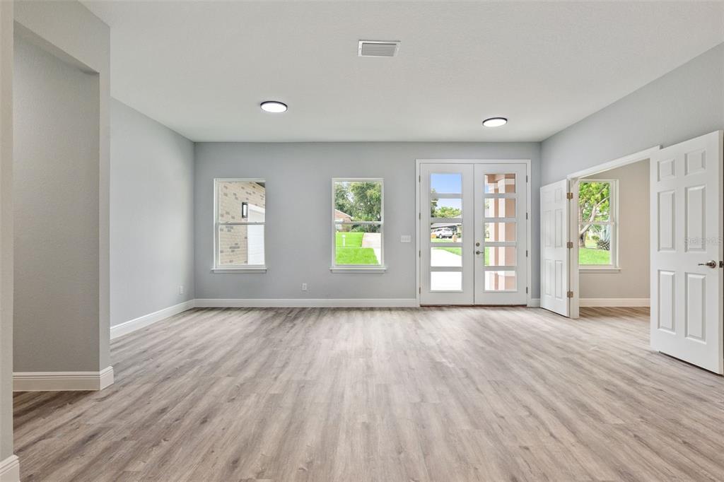 A bright, empty room features light gray walls, wood-look flooring, two windows, and glass-paneled doors — 2043 WATERSEDGE DRIVE, DELTONA, FL