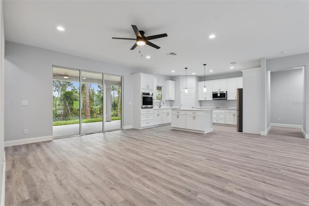 An open-concept kitchen and living area features white cabinetry, a center island, and sliding doors — 2043 WATERSEDGE DRIVE, DELTONA, FL