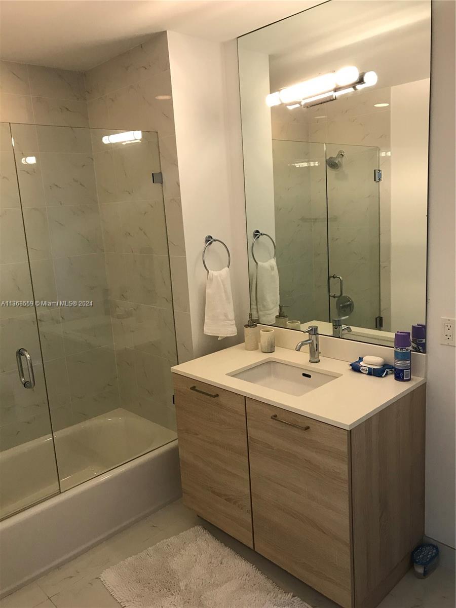 A modern bathroom features a light wood vanity, a white countertop, and a glass-enclosed shower — 16385 Biscayne Blvd # 7, North Miami Beach FL 33160, NORTH MIAMI BEACH, FL