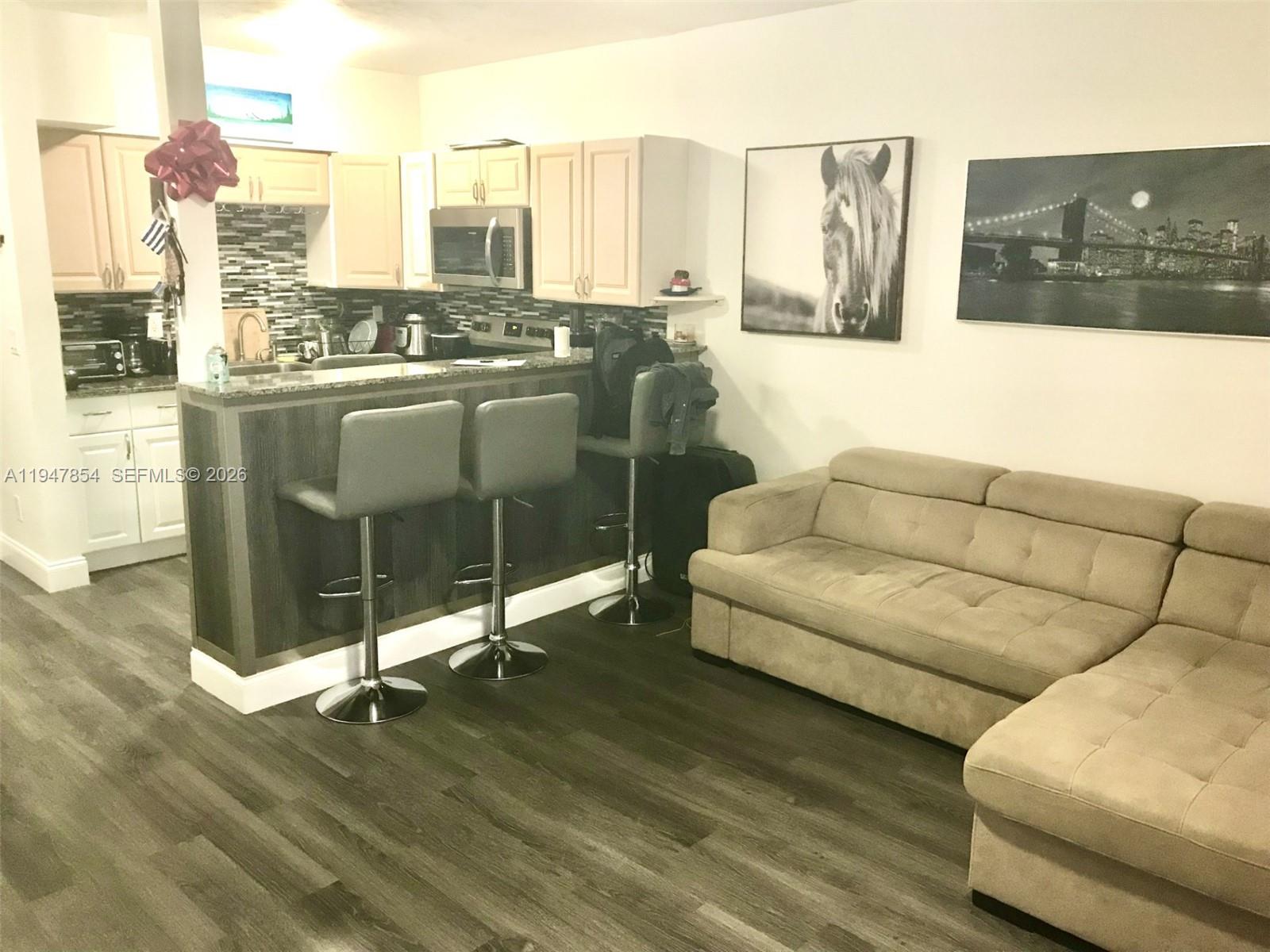 A kitchen with light cabinets and a breakfast bar sits next to a beige sofa — 900 SW 11th Ave # 7C, Hallandale Beach FL 33009, HALLANDALE BEACH, FL