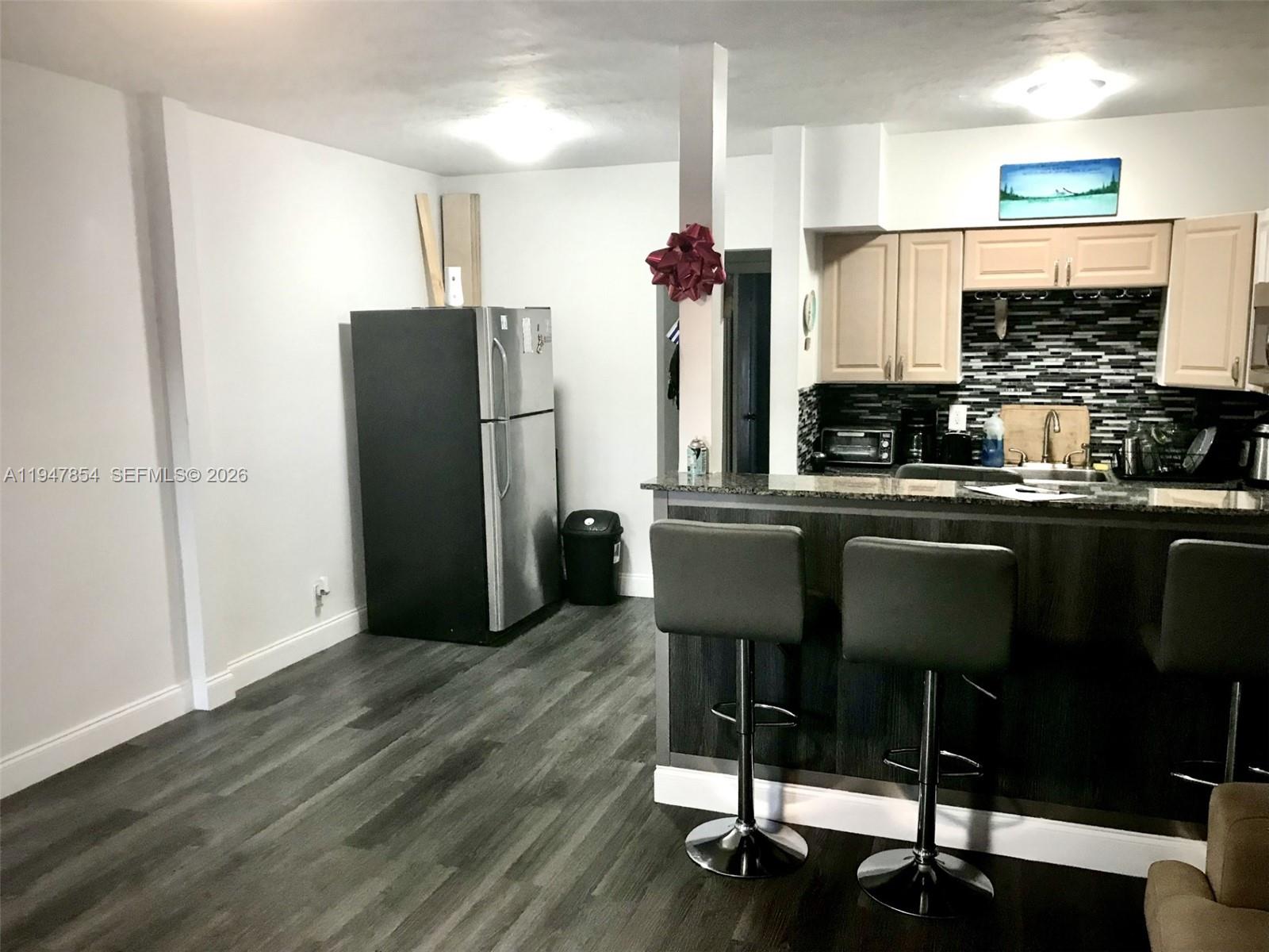 A kitchen features a stainless steel refrigerator, dark wood bar seating, and light-colored cabinets — 900 SW 11th Ave # 7C, Hallandale Beach FL 33009, HALLANDALE BEACH, FL
