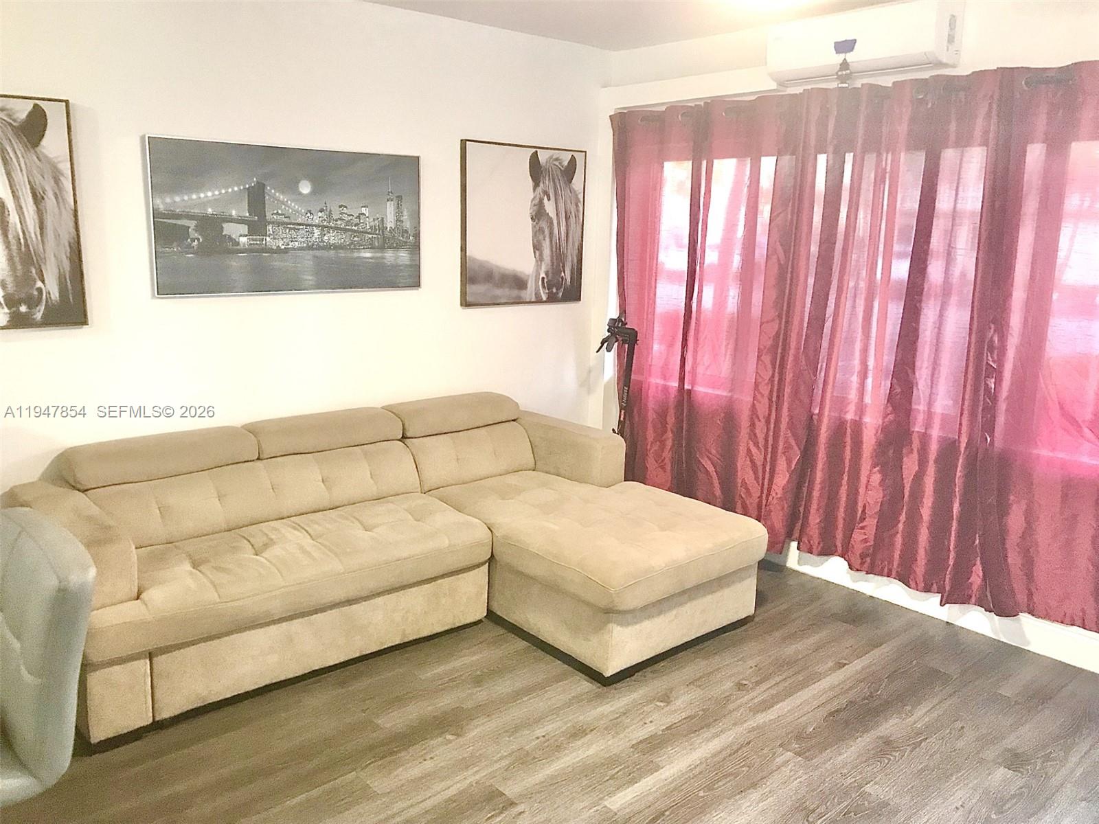 A living room features a beige sectional sofa, wall art, and red curtains — 900 SW 11th Ave # 7C, Hallandale Beach FL 33009, HALLANDALE BEACH, FL