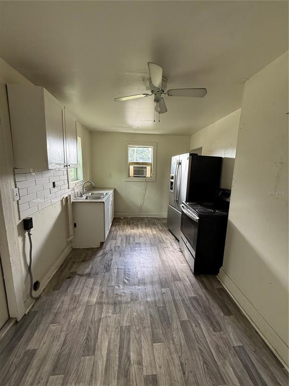 A narrow kitchen features white cabinets, a stainless steel refrigerator, a black stove, and wood-look flooring — 2712 E COLUMBUS DRIVE, TAMPA, FL