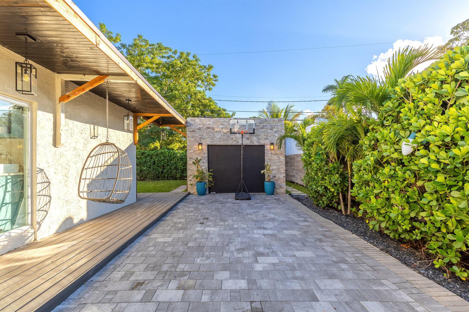 A paved driveway leads to a stone-faced garage with a basketball hoop in a backyard — 726 Lytle Street, West Palm Beach FL 33405, WEST PALM BEACH, FL