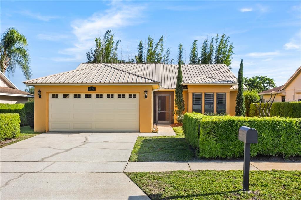 A single-story yellow house with a metal roof, two-car garage, and manicured hedges — 5332 DORRINGTON LANE, ORLANDO, FL
