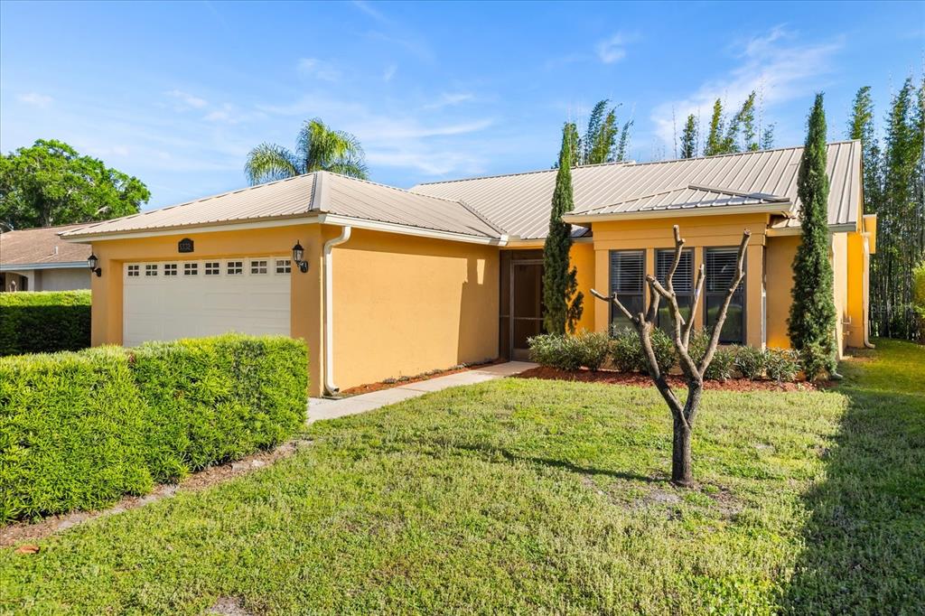 A single-story yellow house with a metal roof, a two-car garage, and manicured landscaping — 5332 DORRINGTON LANE, ORLANDO, FL