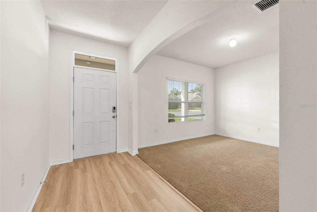 An entryway with wood-look flooring leads into a carpeted room with a window — 8008 SW 62ND COURT, GAINESVILLE, FL