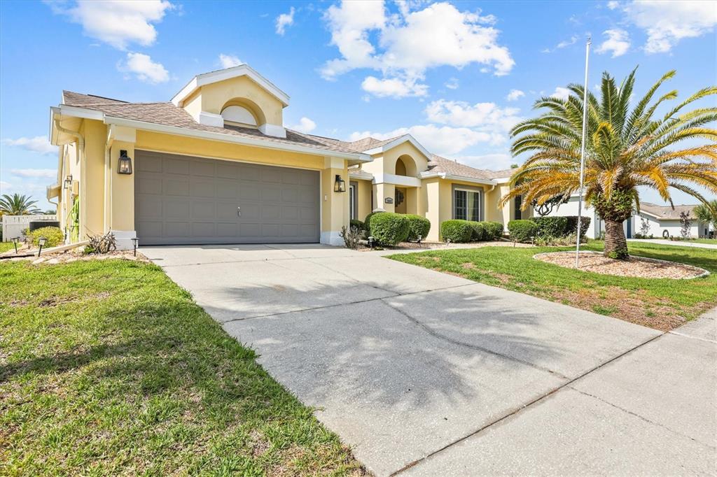 A yellow single-story house features a two-car garage, a concrete driveway, and a palm tree — 1049 LARKIN ROAD, SPRING HILL, FL