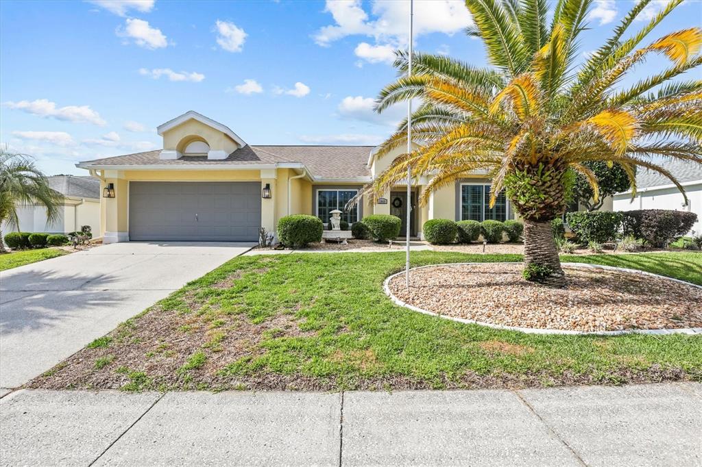 A yellow single-story house features a gray garage, a palm tree, and a landscaped yard — 1049 LARKIN ROAD, SPRING HILL, FL