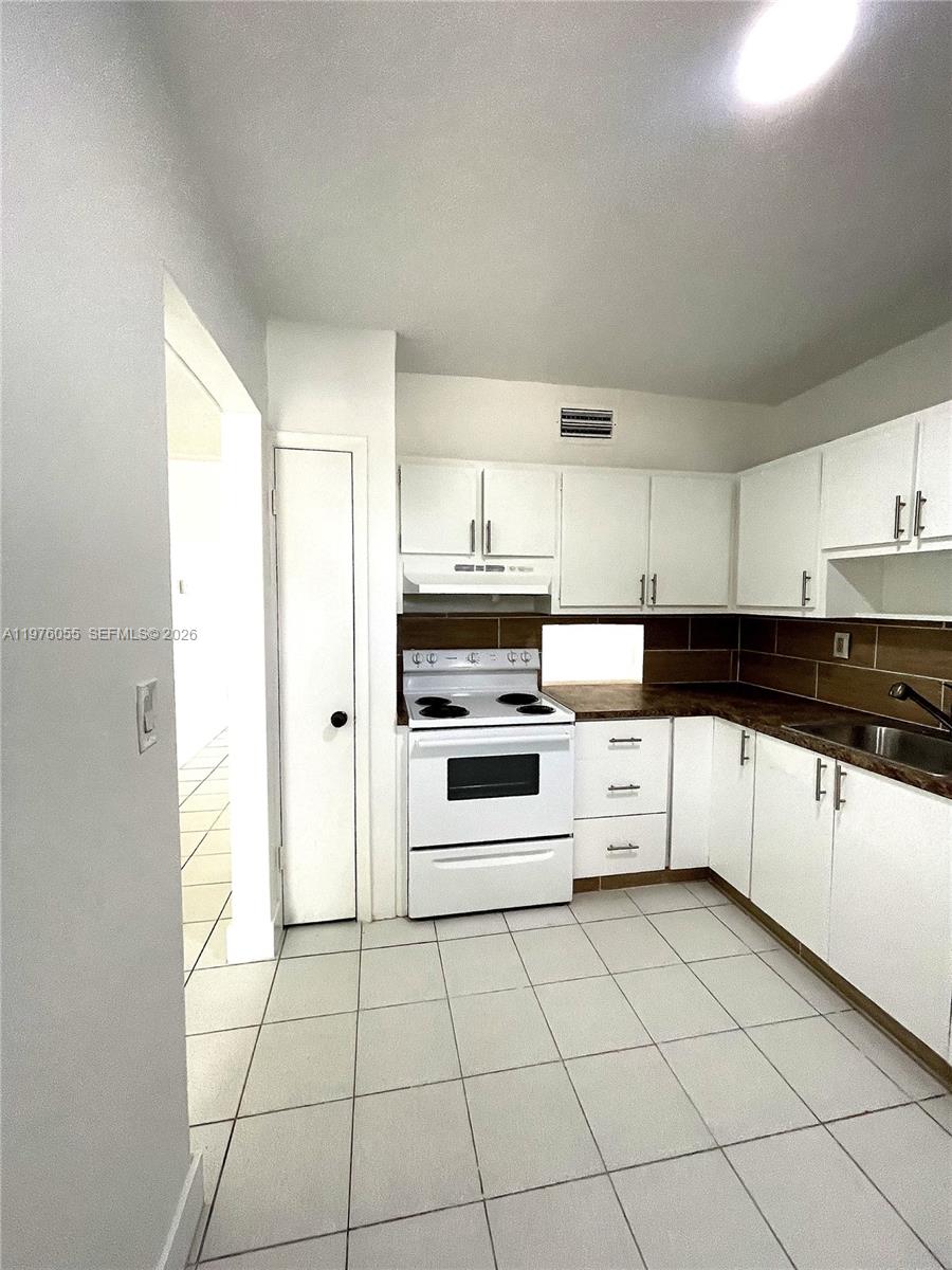 A kitchen features white cabinets, a white stove, dark countertops, and light-colored floor tiles — 19255 NE 2nd Ave # 2224, Miami FL 33179, MIAMI, FL