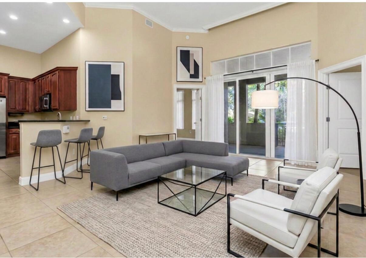 A living room with a grey sectional, glass coffee table, and two white armchairs — 16102 Emerald Estates Drive # 108, Weston FL 33331, WESTON, FL