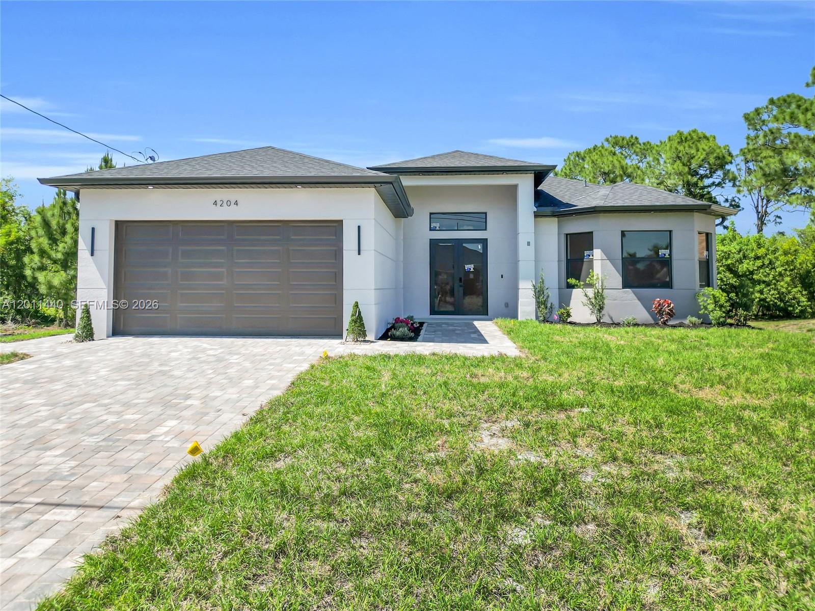 A modern single-story house features a gray garage door, white exterior, and a paved driveway — 4204 3RD ST W, Lehigh Acres FL 33971, LEHIGH ACRES, FL