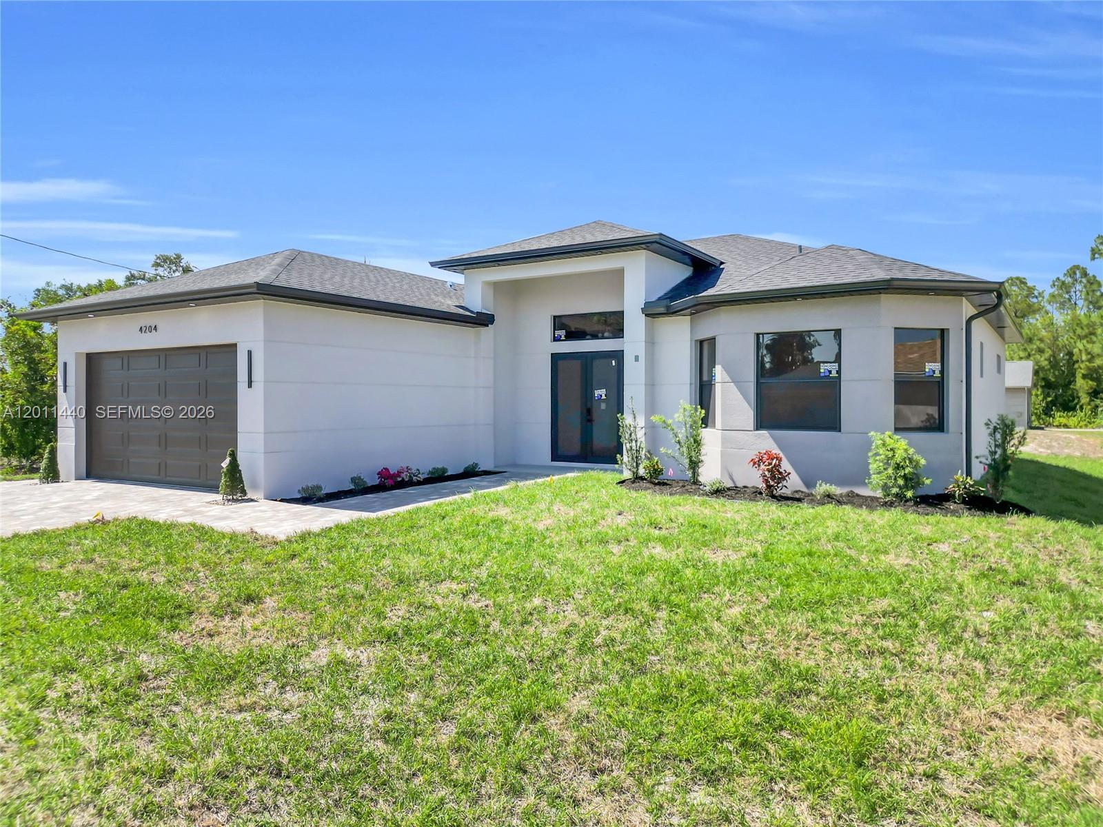 A modern single-story house with a white exterior, dark roof, and a two-car garage — 4204 3RD ST W, Lehigh Acres FL 33971, LEHIGH ACRES, FL