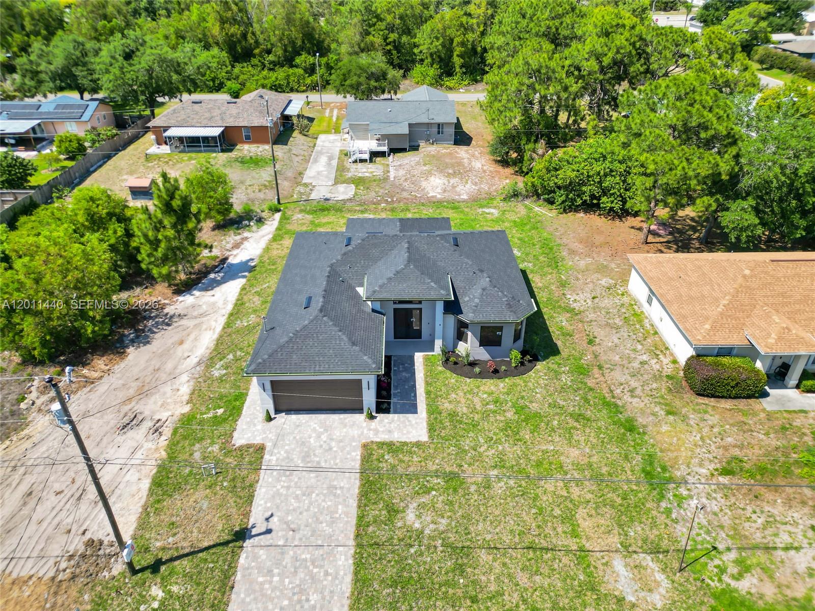 An aerial view shows a modern house with a dark roof and paved driveway — 4204 3RD ST W, Lehigh Acres FL 33971, LEHIGH ACRES, FL