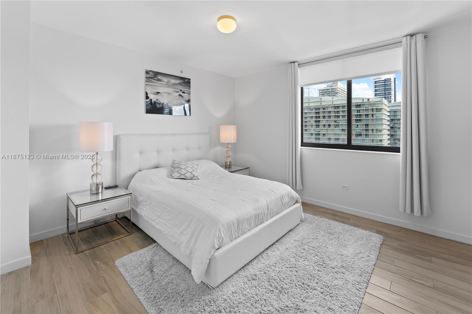 A bedroom features a white bed, two nightstands, a rug, and a window with city views — 999 SW 1st Ave # 3304, Miami FL 33130, MIAMI, FL