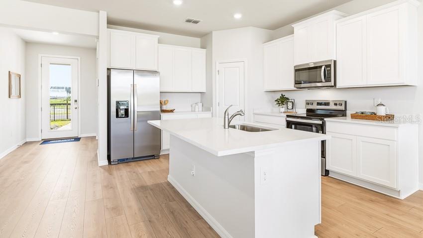 A modern kitchen features white cabinets, stainless steel appliances, and a central island with seating — 10730 RABBIT GROVE TRAIL, PARRISH, FL