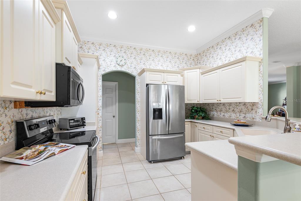 A kitchen with cream cabinets, stainless steel appliances, floral wallpaper, and light-colored tile flooring — 126 LAKE REGION CIRCLE, WINTER HAVEN, FL