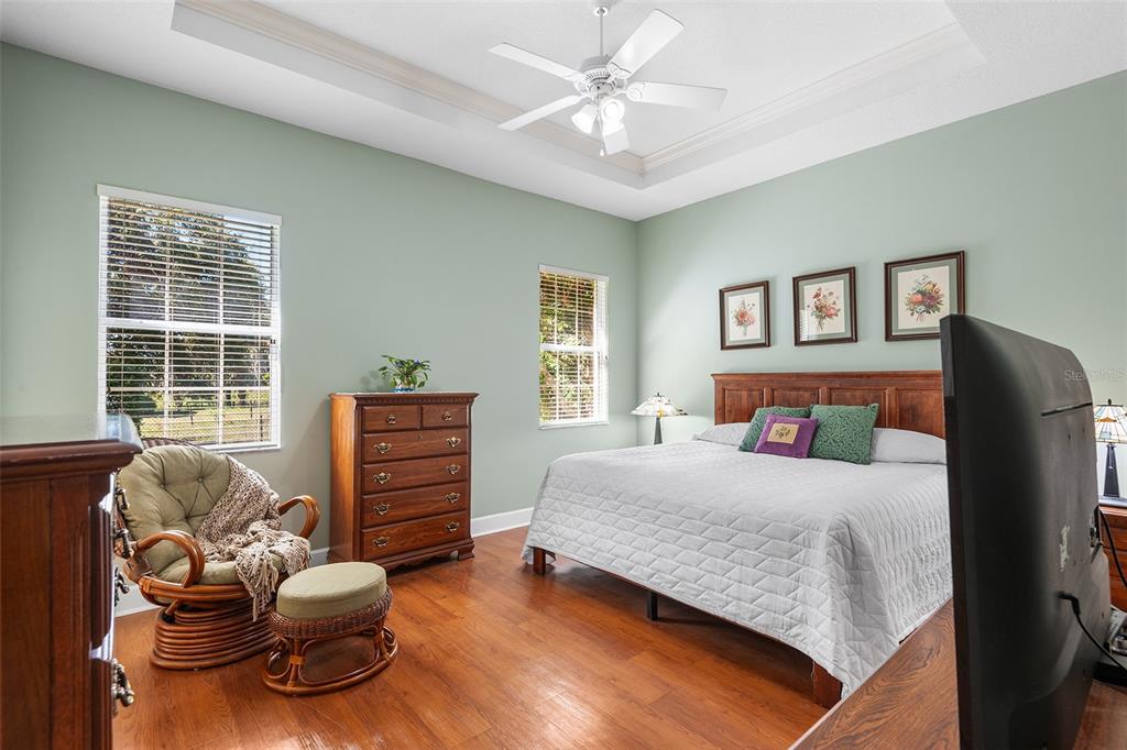 A bedroom with light green walls, wood flooring, a ceiling fan, and a king-sized bed — 126 LAKE REGION CIRCLE, WINTER HAVEN, FL