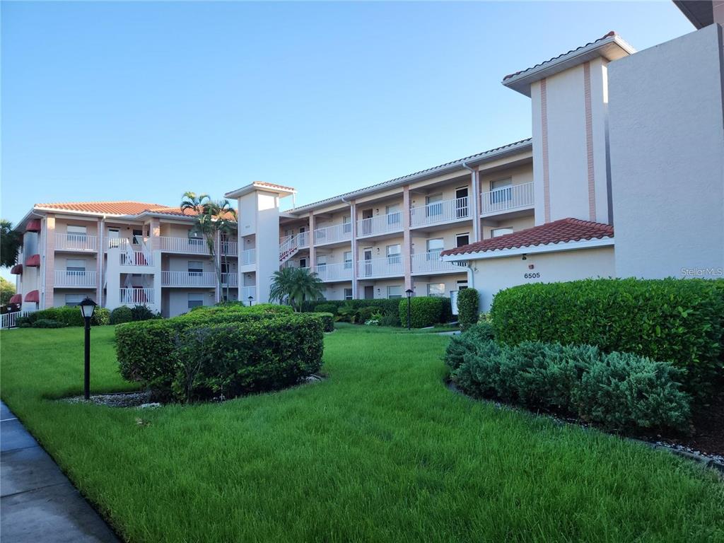 A multi-story apartment building with balconies and a landscaped lawn in the foreground — 6505 STONE RIVER ROAD UNIT 203, BRADENTON, FL